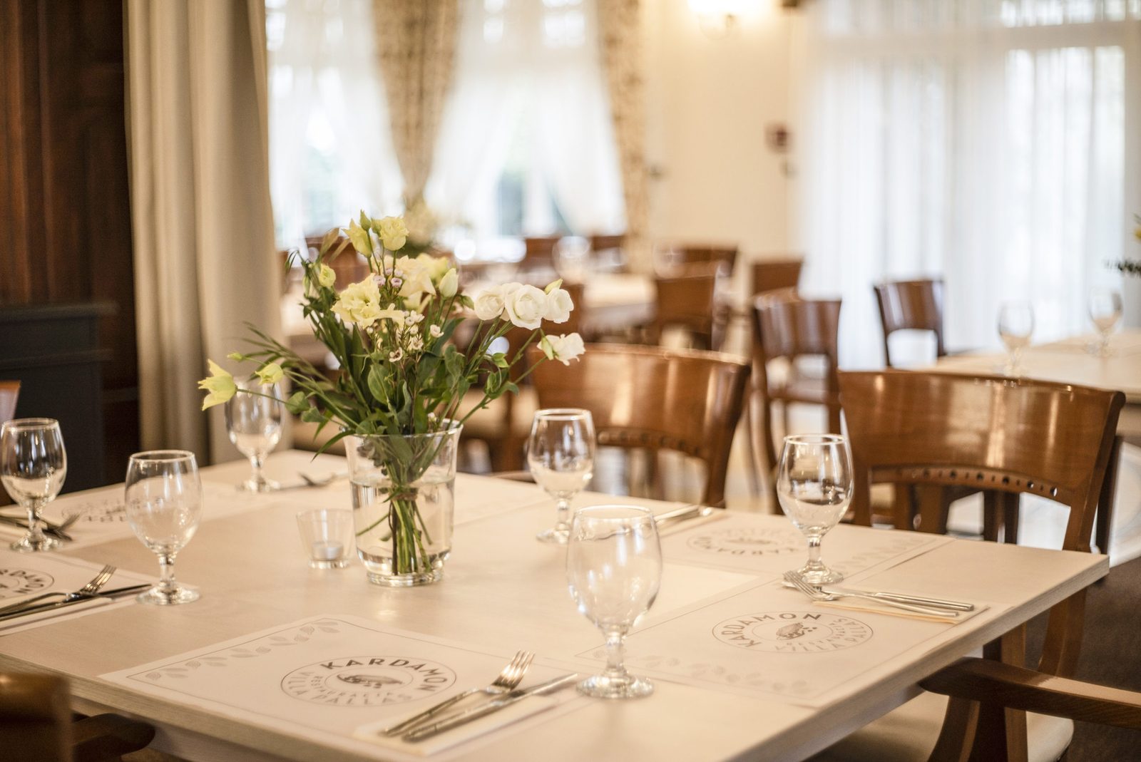 Kardamon dining salon — set table with logo placemats and flowers